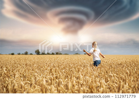 Back view little kid girl walking ripe wheat field imagined nuclear bomb explosion mushroom dramatic cloud background. Natural tornado hurricane disaster. Nuke war strike attack end world concept 112971779