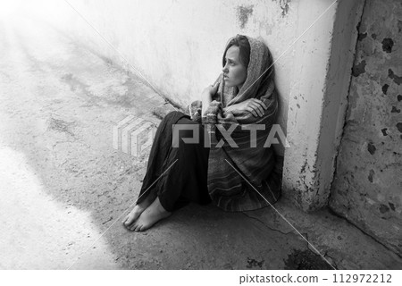 A girl in poor clothes sits on the ground A girl in poor clothes sits on the ground 112972212