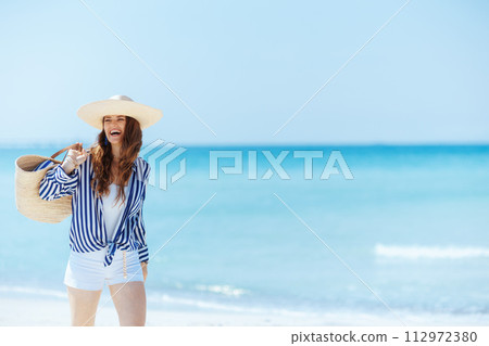 smiling stylish woman on ocean coast with straw bag walking smiling stylish woman on ocean coast with straw bag walking 112972380