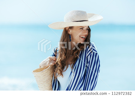 happy stylish woman on seashore with straw bag happy stylish woman on seashore with straw bag 112972382