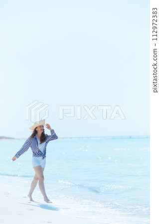 happy elegant female on ocean shore with straw hat walking happy elegant female on ocean shore with straw hat walking 112972383