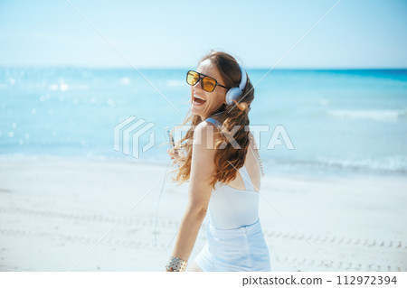 happy stylish woman on seashore with headphones dancing happy stylish woman on seashore with headphones dancing 112972394