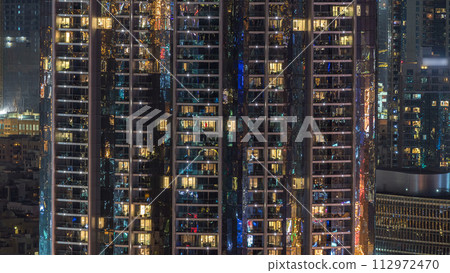 Windows of the multi-storey building of glass and steel lighting inside and moving people within timelapse 112972470