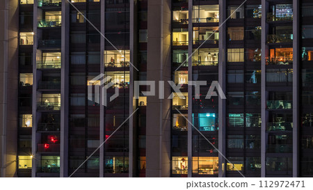 Windows of the multi-storey building of glass and steel lighting inside and moving people within timelapse 112972471