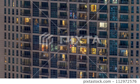 Windows of the multi-storey building of glass and steel lighting inside and moving people within timelapse 112972576