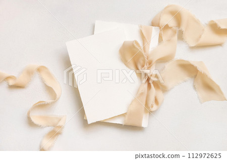 Cards tied with a beige silk ribbon on white table top view, copy space, wedding stationery mockup Cards tied with a beige silk ribbon on white table top view, copy space, wedding stationery mockup 112972625