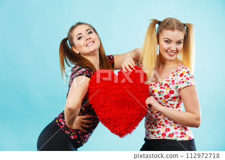 Happy two women holding heart shaped pillow Happy two women holding heart shaped pillow 112972718