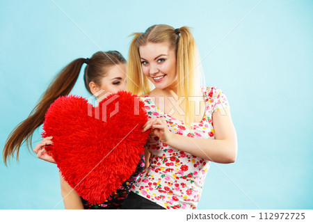 Happy two women holding heart shaped pillow Happy two women holding heart shaped pillow 112972725