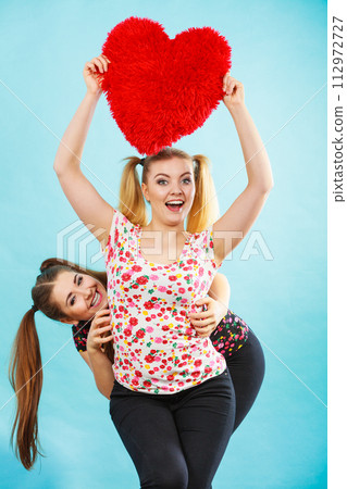 Happy two women holding heart shaped pillow Happy two women holding heart shaped pillow 112972727