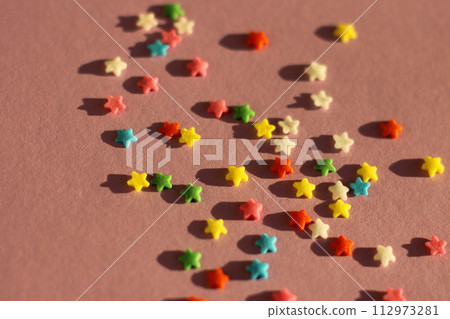 festive pink background with scattered small multicolored stars. confectionery sprinkles 112973281