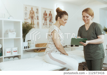 smiling therapist woman doing checkup and writing in clipboard 112973416