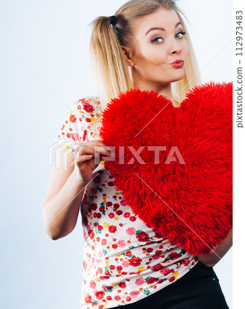 Happy woman holding heart shaped pillow 112973483