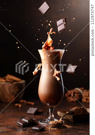Pieces of dark chocolate fall into a glass of cocoa drink. 112973747