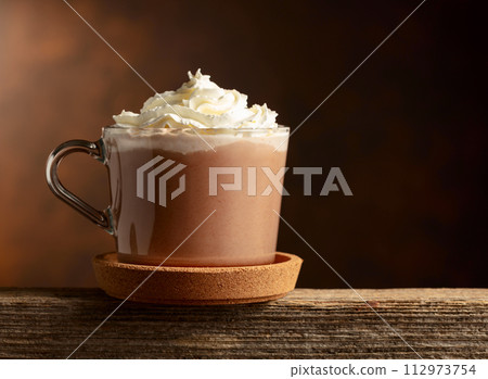 Hot chocolate with whipped cream in a glass mug. 112973754