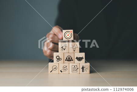 Business goals and target success concepts. Businessman places wooden blocks with business icons. business growth, Achievement company, corporate startup, investment goal, Planning ideas and strategy, Business goals and target success concepts. Businessman places wooden blocks with business icons. business growth, Achievement company, corporate startup, investment goal, Planning ideas and strategy, 112974006