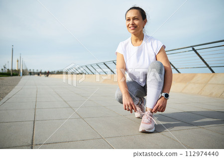 Female runner tying laces on running shoes, ready for jog on the Atlantic promenade on beautiful sunny summer day 112974440