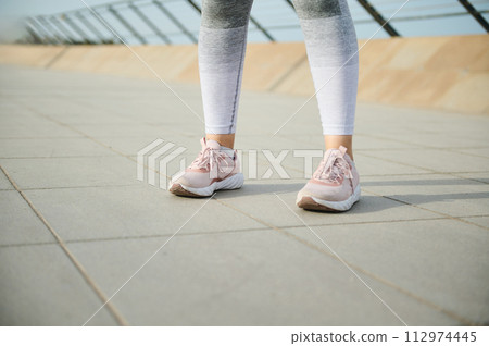 Female legs in pink sneakers running sports shoes and gray leggings on the treadmill on the city bridge. Copy ad space 112974445