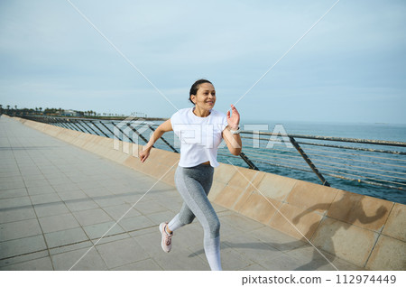 Determined female athlete jogging running on the city bridge during her morning cardio workout on the Atlantic promenade 112974449