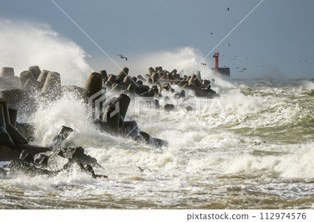 Storm at sea, high waves crashing against the concrete breakwaters of the port, white splashes 112974576