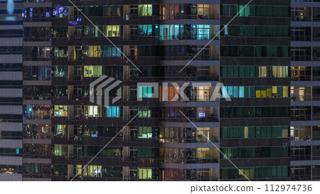 Windows of the multi-storey building of glass and steel lighting inside and moving people within timelapse 112974736