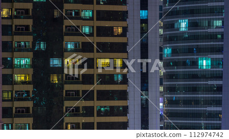 Windows of the multi-storey building of glass and steel lighting inside and moving people within timelapse 112974742