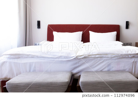 Clean Bedding sheets and pillow on natural wall room background. White bedding and pillow in hotel room. White pillows on empty bed. Clean Bedding sheets and pillow on natural wall room background. White bedding and pillow in hotel room. White pillows on empty bed. 112974896