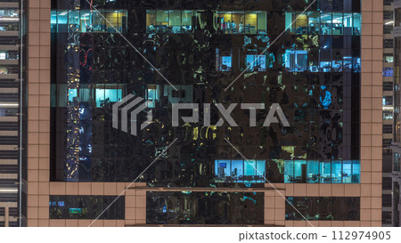 Windows of the multi-storey building of glass and steel lighting inside and moving people within timelapse 112974905