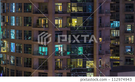 Windows of the multi-storey building of glass and steel lighting inside and moving people within timelapse 112974943
