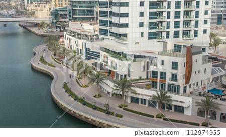 Promenade and canal in Dubai Marina with luxury skyscrapers and yachts around timelapse, United Arab Emirates Promenade and canal in Dubai Marina with luxury skyscrapers and yachts around timelapse, United Arab Emirates 112974955