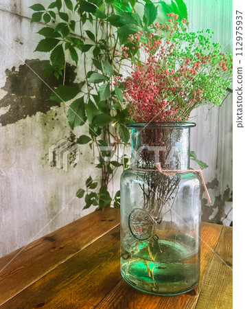 Artificial dry coloured flowers in a large green glass vase as a part of interior design 112975937
