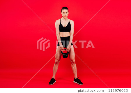 Young female doing swing exercise with a kettle bell. Fitness woman 112976023