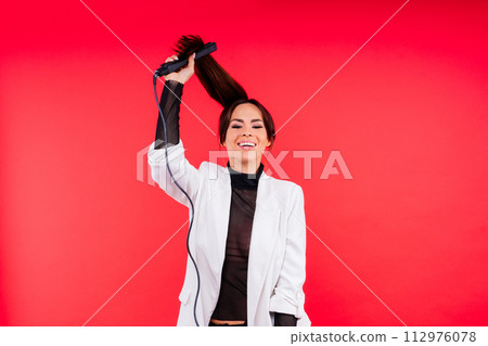 Happy young woman with beautiful hair holding curling iron on grey and red background 112976078