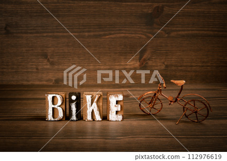 BIKE. Text from alphabet blocks and rusty miniature bicycle on wood texture background BIKE. Text from alphabet blocks and rusty miniature bicycle on wood texture background 112976619