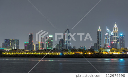 Modern Dubai city skyline timelapse at night with illuminated skyscrapers over water surface Modern Dubai city skyline timelapse at night with illuminated skyscrapers over water surface 112976698