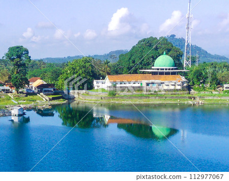 serene lake surrounded by lush green trees, with a white building with a mosque in the background. serene lake surrounded by lush green trees, with a white building with a mosque in the background. 112977067