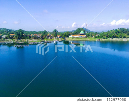 serene lake surrounded by lush green trees, with a white building with a mosque in the background. 112977068