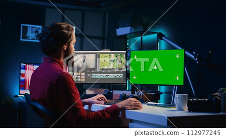 Video editor using editing software on green screen monitor to upgrade footage shot, commissioned by production teams outsourcing tasks. Freelancer videographer finishing project on mockup PC 112977245