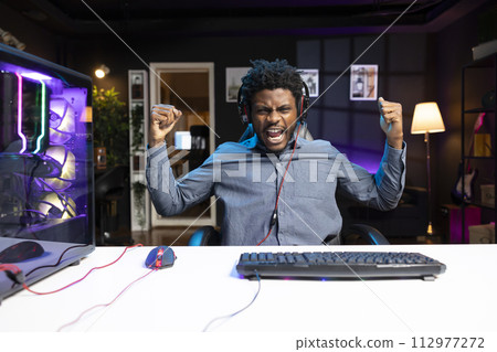 Excited gamer screaming from joy after winning PC game during live stream with viewers. Cheerful player bragging after being victorious in videogame while broadcasting gameplay for fans 112977272
