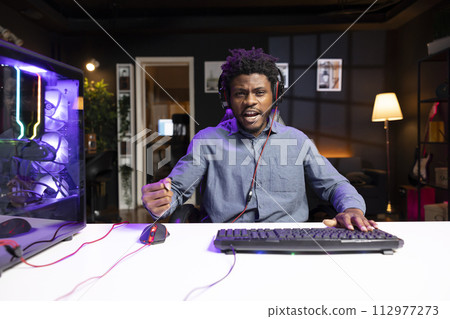 POV of man playing videogames using computer peripherals, celebrating victory. Gamer excited after winning online multiplayer game match on gaming PC, talking with friends through headset 112977273
