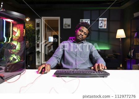 Man playing boring singeplayer videogame, feeling turned off by repetitive enemies and missions. African american gamer in living room struggling to keep interest in game, wearied by grinding 112977276