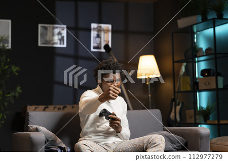 Ecstatic gamer punching air from joy after finally finishing difficult videogame at home. Man feeling relieved and excited after defeating enemies during gaming session on console 112977279