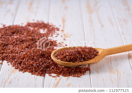Raw red rice crumble from in a wooden spoon on a white wooden table. 112977525