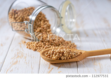 soybeans in wooden scoop and in glass storage jar on a white wooden table. 112977531