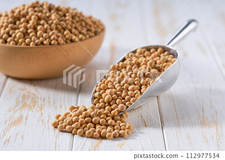 Raw soybeans in a metal scoop on a white wooden table. 112977534