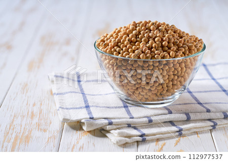 Raw soybeans in a glass plate on a white wooden table. Raw soybeans in a glass plate on a white wooden table. 112977537