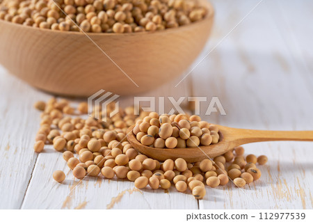 wooden spoon with raw soybeans on a light table, selective focus. wooden spoon with raw soybeans on a light table, selective focus. 112977539