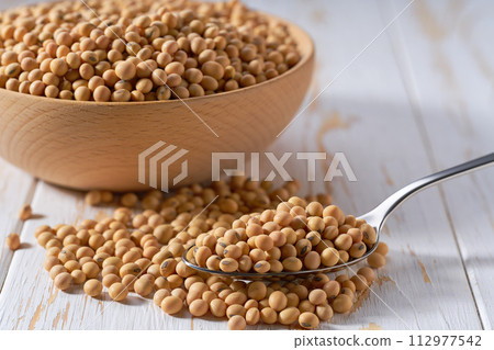 metal spoon with raw soybeans on a light table, selective focus. 112977542