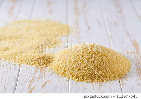 Pile of raw couscous on a white wooden table. Heap of organic couscous on a white wooden table. Pile of raw couscous on a white wooden table. Heap of organic couscous on a white wooden table. 112977543