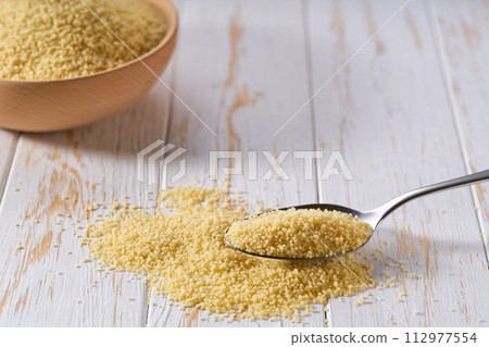 metal spoon with organic couscous on a white wooden table. metal spoon with organic couscous on a white wooden table. 112977554