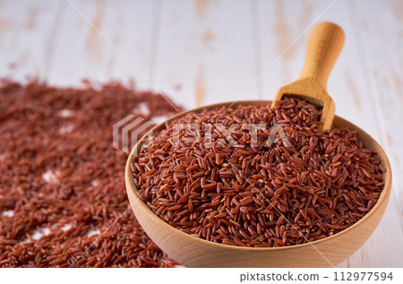 Raw red rice are scattered in a wooden bowl close up. 112977594